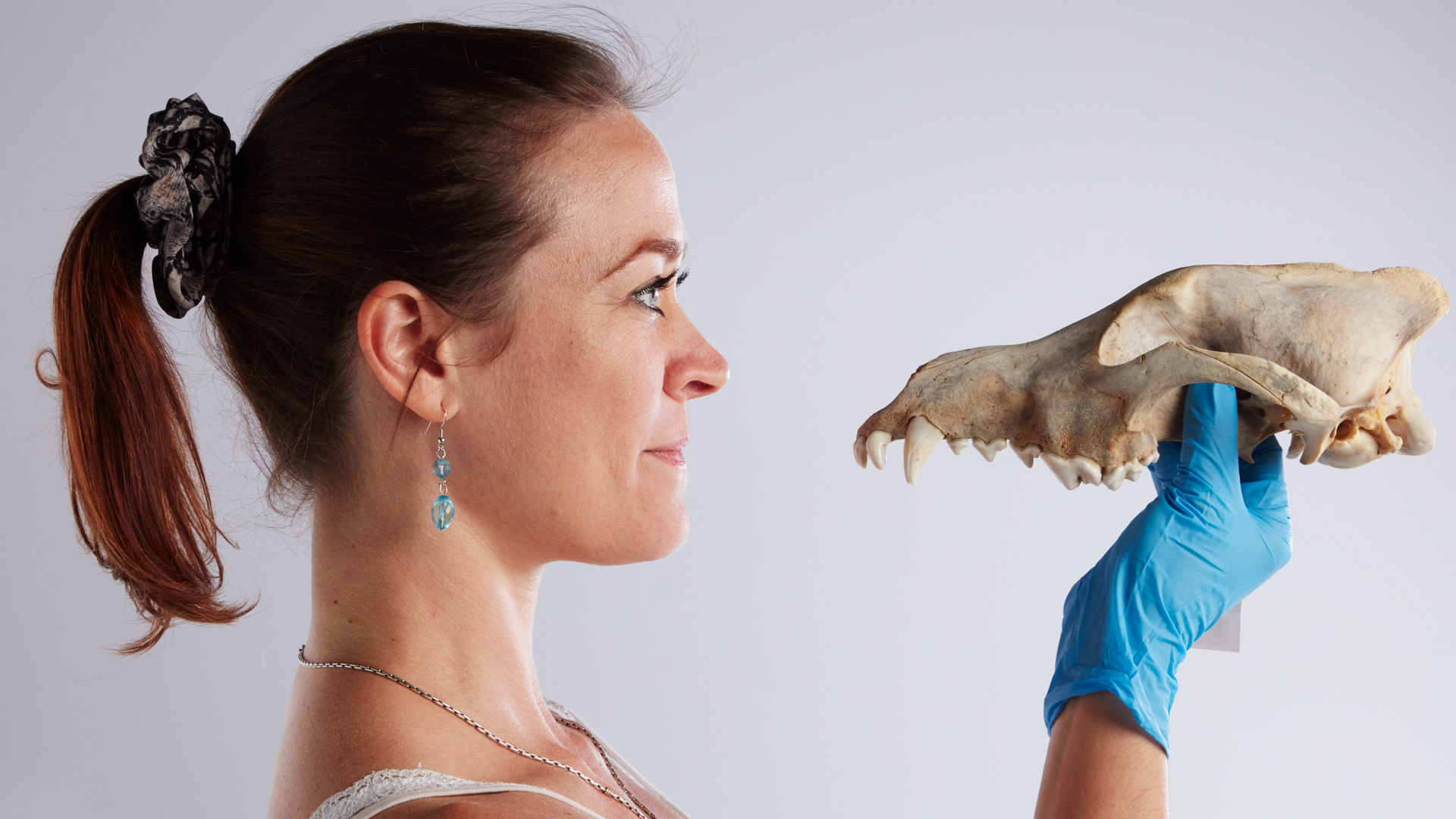 Woman holding up a wolf skull so that she is looking directly at it.
