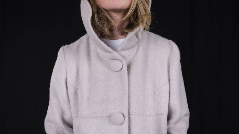 A close up image of a person wearing a buttoned up faux fur coat with a hood.