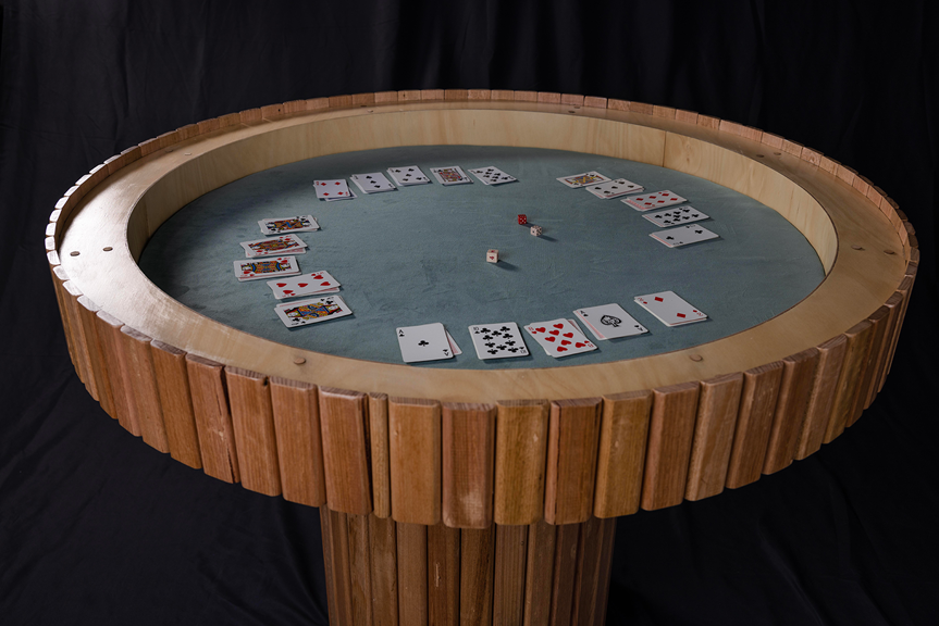 A circular wooden table with an open top. Inside the table is a dark green fabric surface with a deck of cards and dice placed on it.