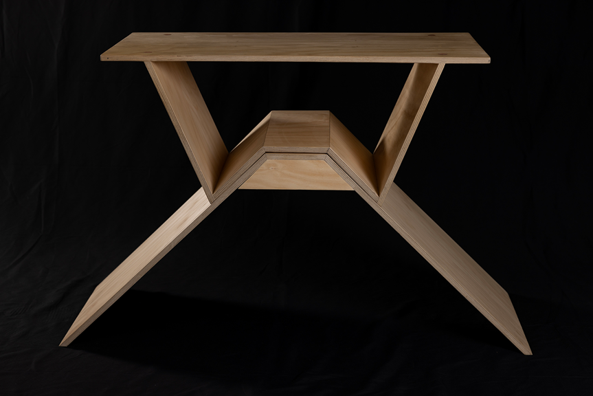 A plywood timber table with angled legs, set against a black background.