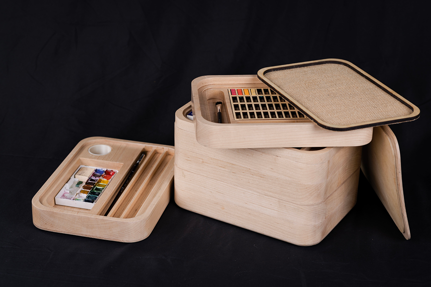 A rectangular wooden box with stackable layers, which contain paints and paintbrushes.