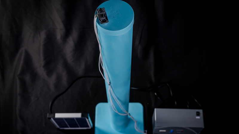 A light blue cylindrical object with a chip and wiring at the top, and two rectangular boxes on both sides.