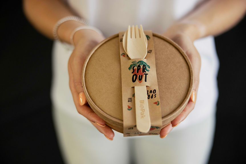 A person holding a takeaway bowl and a set of BioPak cutlery. The packaging is branded with a logo reading ‘Sprout’.
