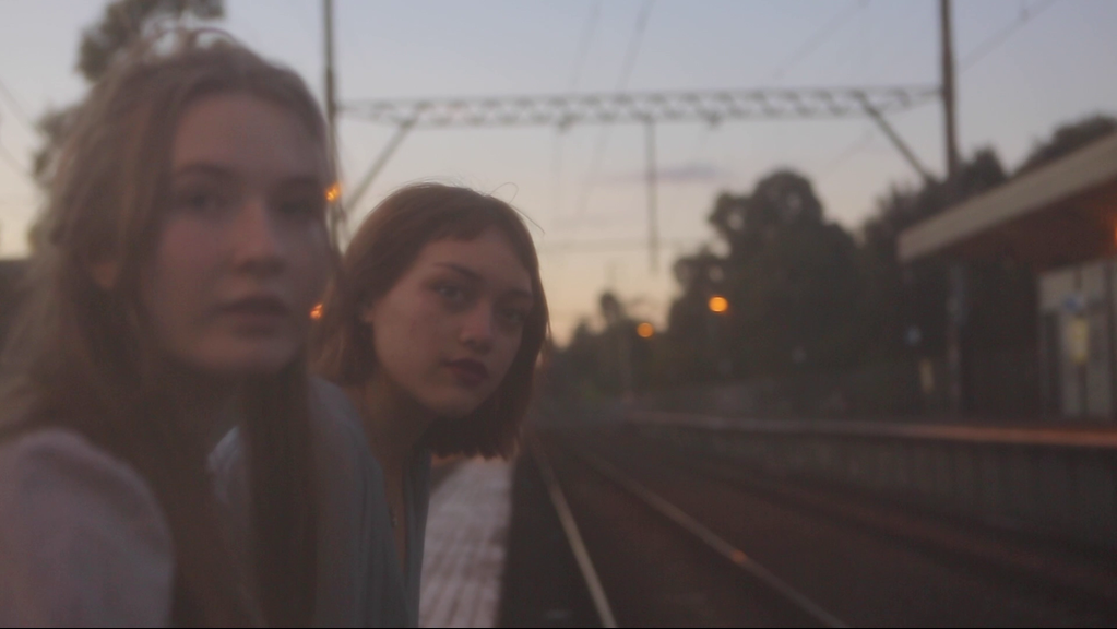 Two young girls sitting at the end of a train stop, looking along the train tracks.