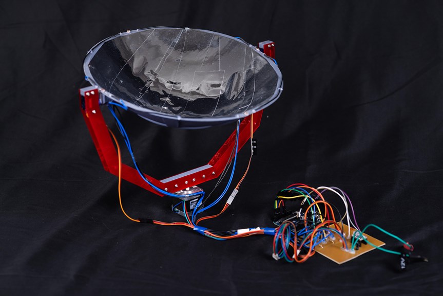 	 A mirrored concave dish supported by a red u-shaped frame and attached at the base to a small stepper motor. Thin blue and red wires run from the mirrored dish to a circuit board.