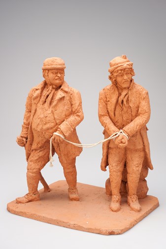 Clay sculpture of two men; one man has his hands bound and is being led by the other