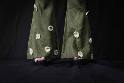 A close up photograph of the final product, showing the bottom of wide trouser legs. The trousers are olive green and have knitted daisies attached.