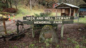Plaque on a rock stands in a small reserve, in front of a shelter and picnic table. 