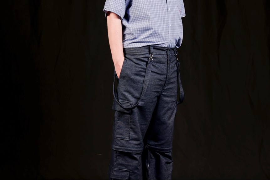 Person wearing a short sleeved blue checked shirt and denim cargo pants with suspenders.