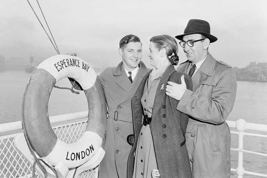 Two men and a woman (a son with his mother and father) standing in front of a white railing. To the left of the picture is a life preserver ring with the words “London / Esperance Bay” printed on it. 