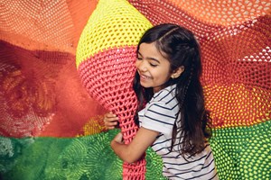 Girl in a climbing net holding onto a rope sculpture