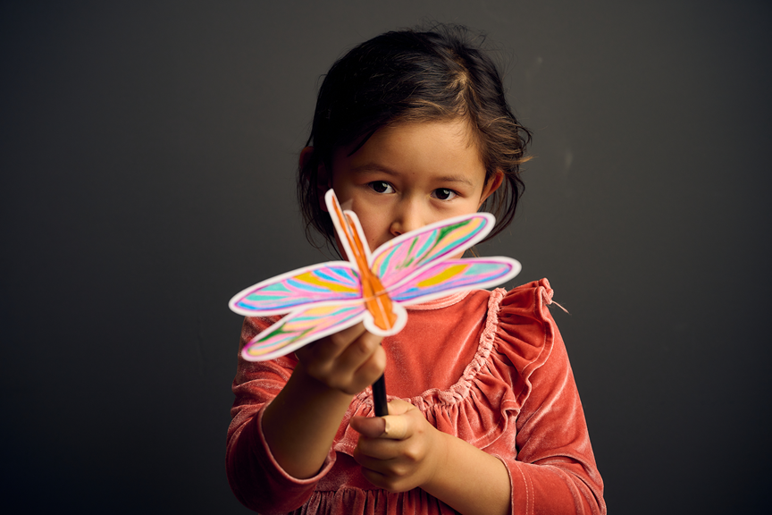 A child holds their colourful dragonfly creation.