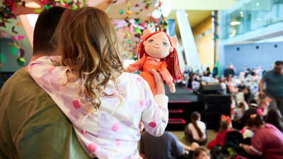 A child holding an Emma Memma doll while watching Emma Memma perform at Melbourne Museum.