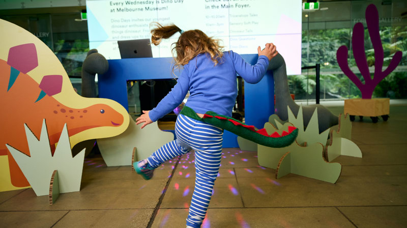 A child wearing a dinosaur tail dancing.