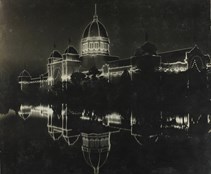 Exhibition Building decorated with lights at night, lake in foreground.