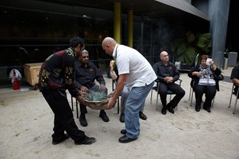 Two men carrying a bowl of smoking eucalyptus leaves