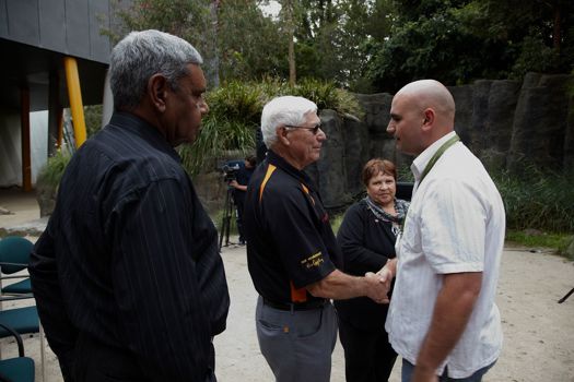 Two men shake hands. A man and a woman look on.