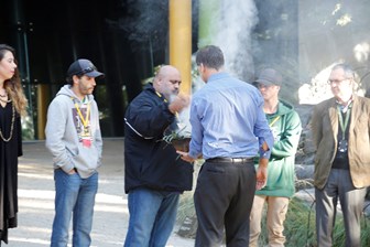 People looking on at a man holding a small bowl of smoke