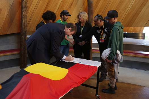 Man signing documents. Five people look on.