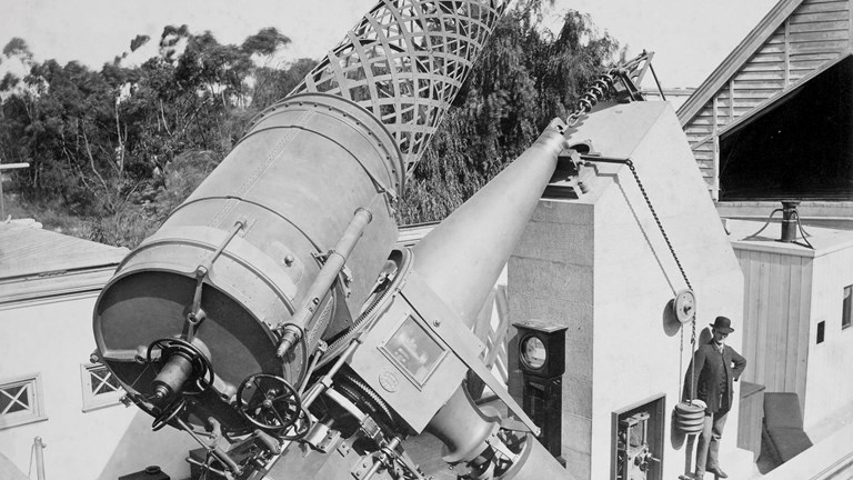 Black and white image of a man standing next to a telescope