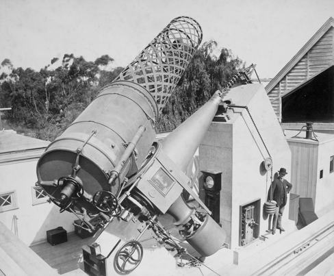 Black and white image of a man standing next to a telescope
