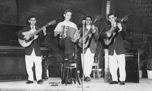 Group of four men; one playing accordion and three playing guitar.