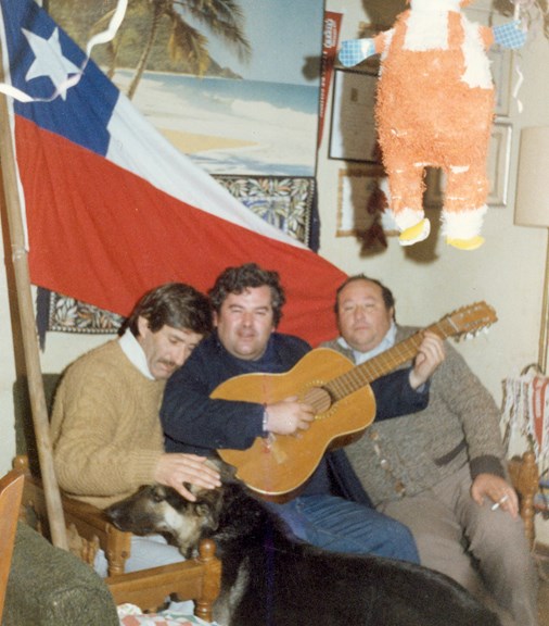 Three men sitting on a sofa. One is playing the guitar