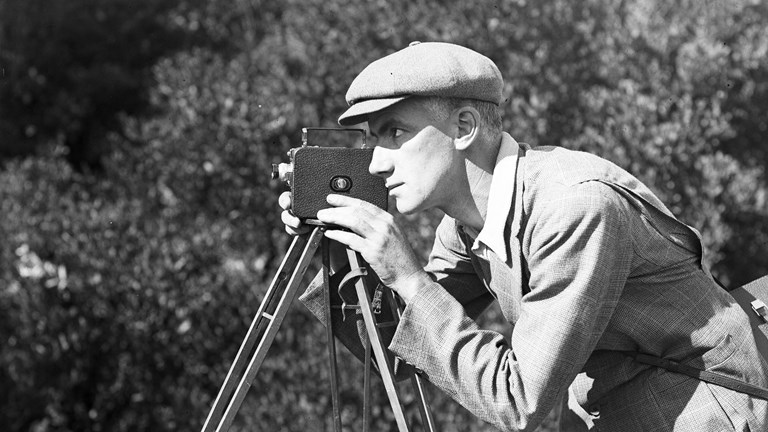 Black and white photograph of a man looking through a movie camera
