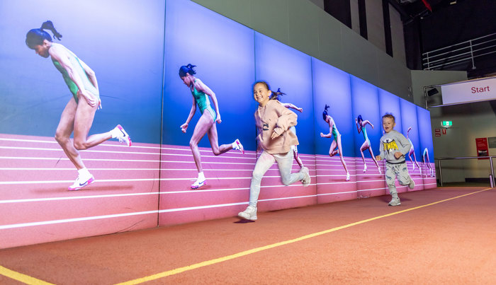 Child trying to run faster than Kathy Freeman in the Sportsworks exhibition during Science is a Superpower festival at Scienceworks.