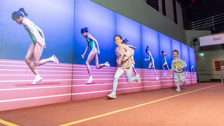 Child trying to run faster than Kathy Freeman in the Sportsworks exhibition during Science is a Superpower festival at Scienceworks.