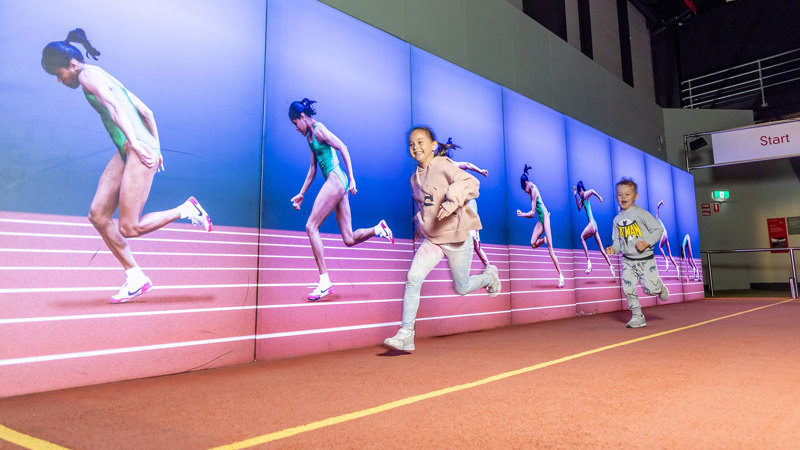 Child trying to run faster than Kathy Freeman in the Sportsworks exhibition during Science is a Superpower festival at Scienceworks.