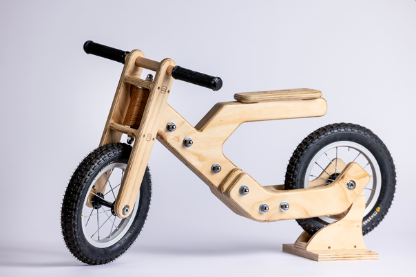 Plywood balance bike with black tyres.