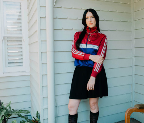 Elle Young, aka DJ Frida, in a black skirt and sports jersey in front of a weather board home.