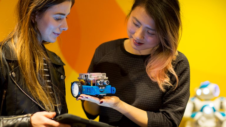 Two women using a computer tablet to program robots