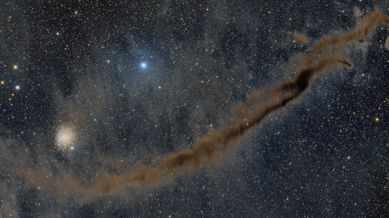 Image of stars from afar with a long line of cloud that is coloured brown.  
