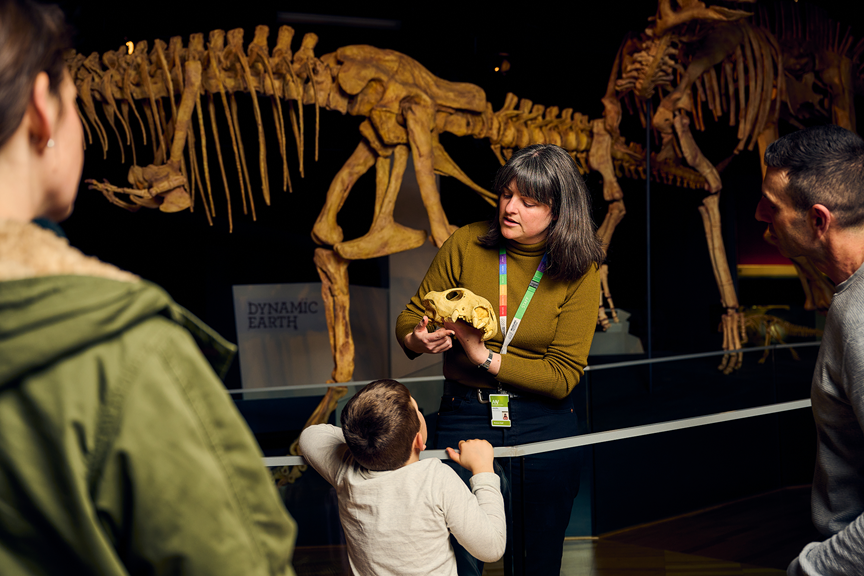 A museum paleontologist shows a fossil to children and their guardians. 