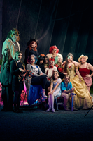 A group of people dressed up in assorted Halloween costumes pose in front of the formidable forest.