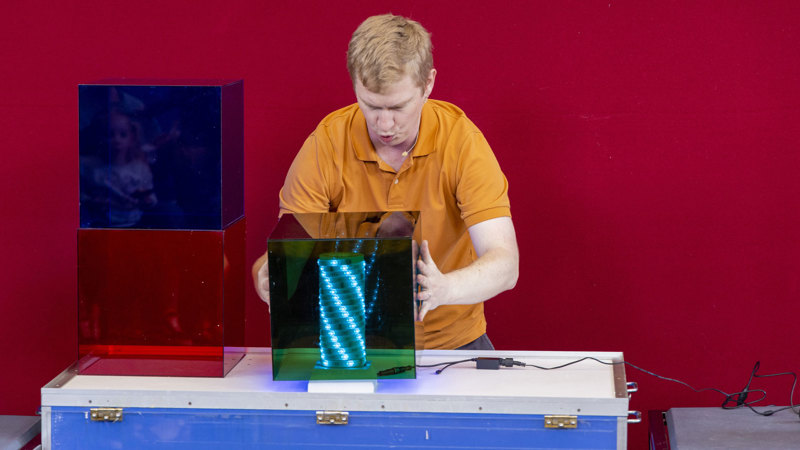 A presenter has their hands around a transparent green box with blue coloured lights inside