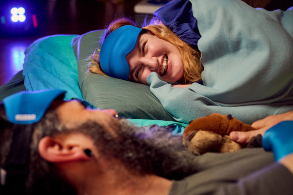 A woman smiling while sleeping under the dinosaurs during Adult Museum Sleepovers at Melbourne Museum.