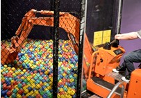 A child operating a bulldozer which is picking up plastic balls from an enclosed cage