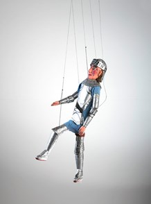 Marionette depicting a mediaeval knight, wearing cardboard armour on his arms, legs, feet and torso, with a matching hat