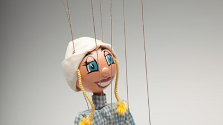 Marionette depicting a girl dressed in a blue and white plaid blouse, pink skirt, white apron and a peasant hat.