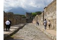 Visitors walking down a Pompeii street, at the end of which stands the Tower of Mercury. Vesuvius is in the background.