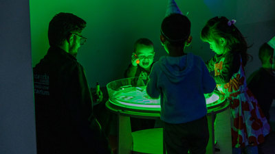 Three children and an adult learning and playing with a glowing light table. 