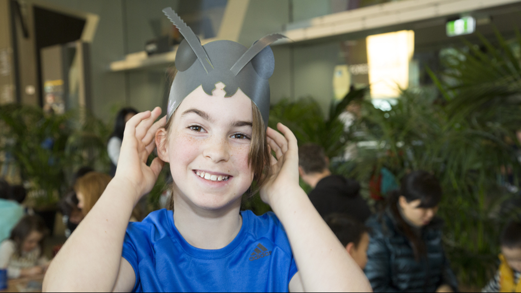 A child wearing an ant antennae headband in the main foyer at the Melbourne Museum.