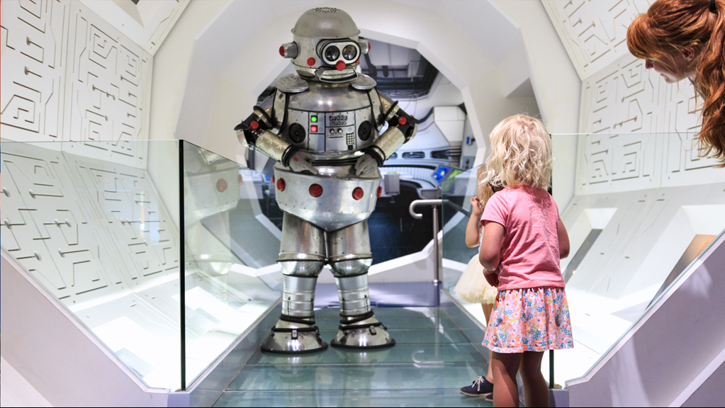  Tubby the Robot shaking hands with a young girl in the Space Station Tunnel in the Think Ahead Exhibition, during the celebrations for 25 years of Scienceworks. Another girl looks on.