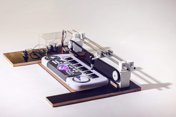 Electronic music device on wooden base featuring a white synthesiser keyboard with illuminated controls, connected to visible circuit boards.