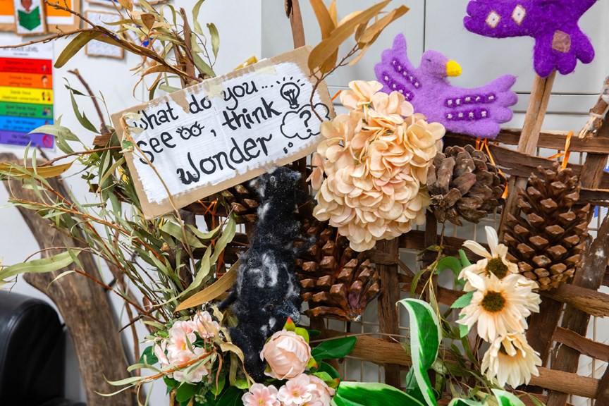 Flowers and pinecones make a diorama. A sign reads 'What do you... See? Think? Wonder?