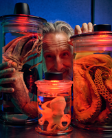 A Museum expert poses behind three preservation jars housing squid and octopi.