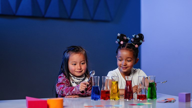 Two preschool age children playing with beakers of colour liquid 